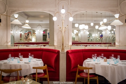 Interior of Benoit New York with deep red banquettes, tables, and mirrors reflecting the dining room's ambiance.