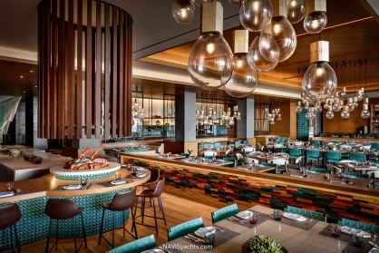 The warm and elegant interior of La Mar by Gastón Acurio, featuring the open cebiche bar, clean lines, and a view of the terrace overlooking the Skyblaze fountain at Atlantis The Royal.