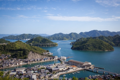 A panoramic view of the Seto Inland Sea at dawn, showing calm waters dotted with numerous green, mountainous islands under a soft sky.