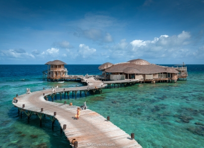 The overwater dining complex "Out of the Blue" at Soneva Fushi, showcasing its two-story structure with open-air design, thatched roof, and integration with the turquoise waters of the Baa Atoll.